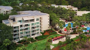 A multi-story hotel with a pool area, outdoor seating, and lush landscaping.