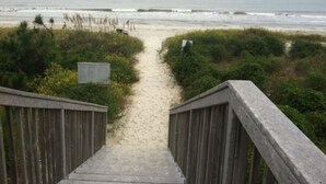 A wooden staircase leading to a sandy beach with a view of the ocean.