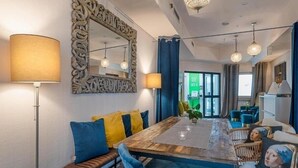 Ein moderner Essbereich mit einem Holztisch, blauen und gelben Kissen und einem großen, verzierten Spiegel.