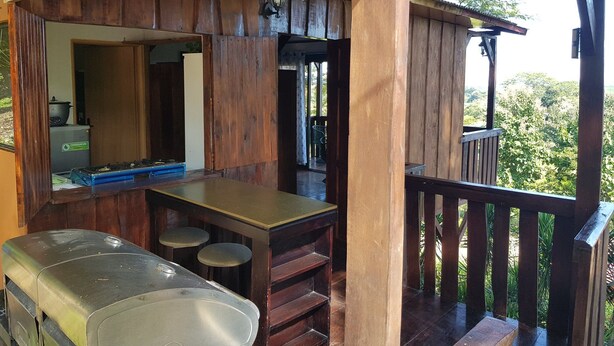 A rustic wooden bar area with a counter and stools, a sink, and a view of the surrounding greenery. - Cabana Luna (Jicaral)
