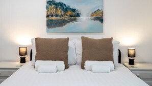 Un letto rifatto con due cuscini marroni e due asciugamani bianchi, affiancato da due comodini con lampade, e un quadro raffigurante un paesaggio sopra il letto.