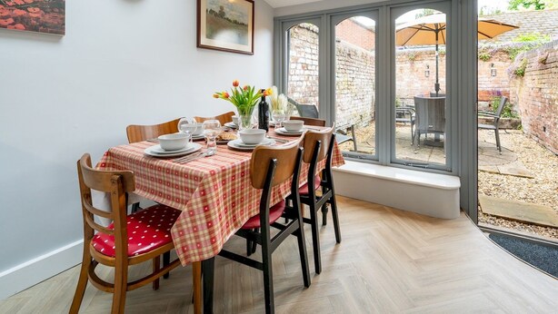 Zona pranzo con tavolo imbandito per quattro persone, un quadro appeso e vista sul giardino attraverso ampie finestre.