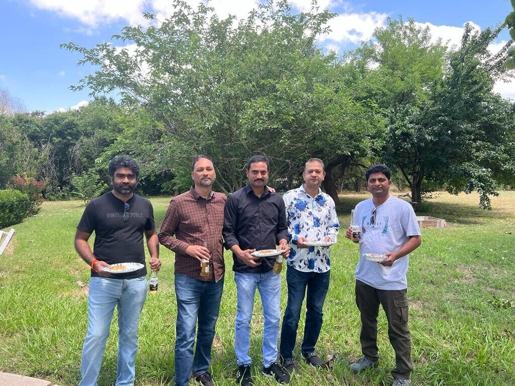 A group of five people standing outdoors in a grassy area with trees in the background.