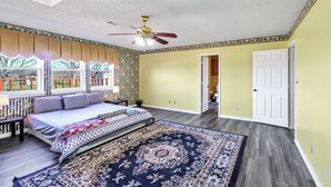 A bedroom with a bed, a ceiling fan, a window with a view, and a door leading to another room.