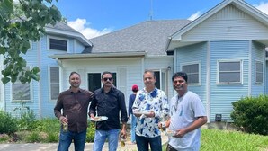 Four people standing in front of a house with a front yard.