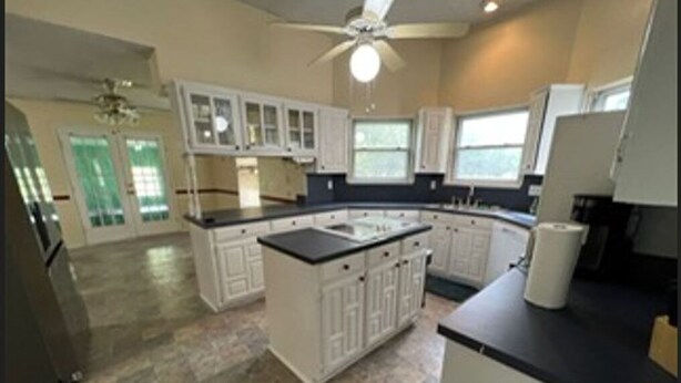 A spacious kitchen with white cabinetry, a central island, and a ceiling fan.