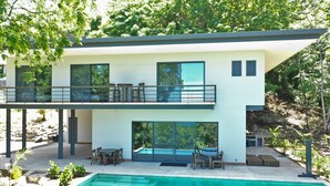 A modern two-story house with a swimming pool, outdoor seating, and a balcony.