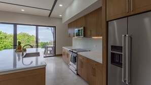 A modern kitchen with stainless steel appliances, wooden cabinets, and a large window offering a view of greenery.