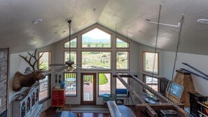 A spacious loft with a high ceiling, large windows offering views of the outdoors, a mounted deer head, and a rustic wooden bench. - Breathtakingly charming 4-bedroom house with WiFi in Charlo. (Charlo)