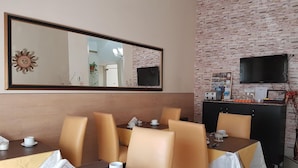 Un espace repas avec des tables et des chaises, un grand miroir, un téléviseur et un mur en briques.