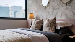 A neatly made bed with striped pillows, a bedside lamp, and a view of buildings through a window. - Sleek High-Rise with Pool, Gym, Jacuzzi & BBQ Area (Mexico City)
