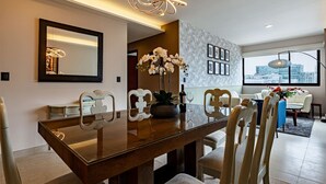 A modern dining area with a wooden table, white chairs, and a city view through large windows. - Sleek High-Rise with Pool, Gym, Jacuzzi & BBQ Area (Mexico City)