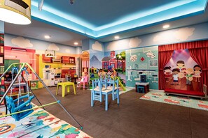 Une salle de jeux pour enfants avec une cuisine miniature, une scène et une fresque murale sur le thème de l’école.