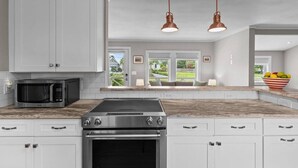 A kitchen with white cabinets, a stainless steel stove, a microwave, and two pendant lights. - Serenity on Trinity - Hot Tub - Pets Welcome (Wilmington)
