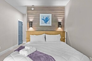 A bedroom with a bed, a blue door, a wooden headboard, and a framed artwork on the wall.