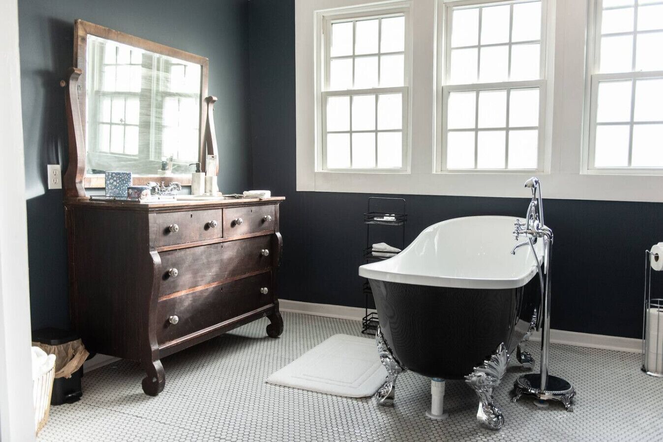 Een badkamer met een donkere muur, een witte badkuip, een houten dressoir en een grote spiegel.