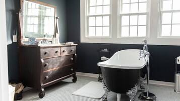 Een badkamer met een donkere muur, een witte badkuip, een houten dressoir en een grote spiegel.