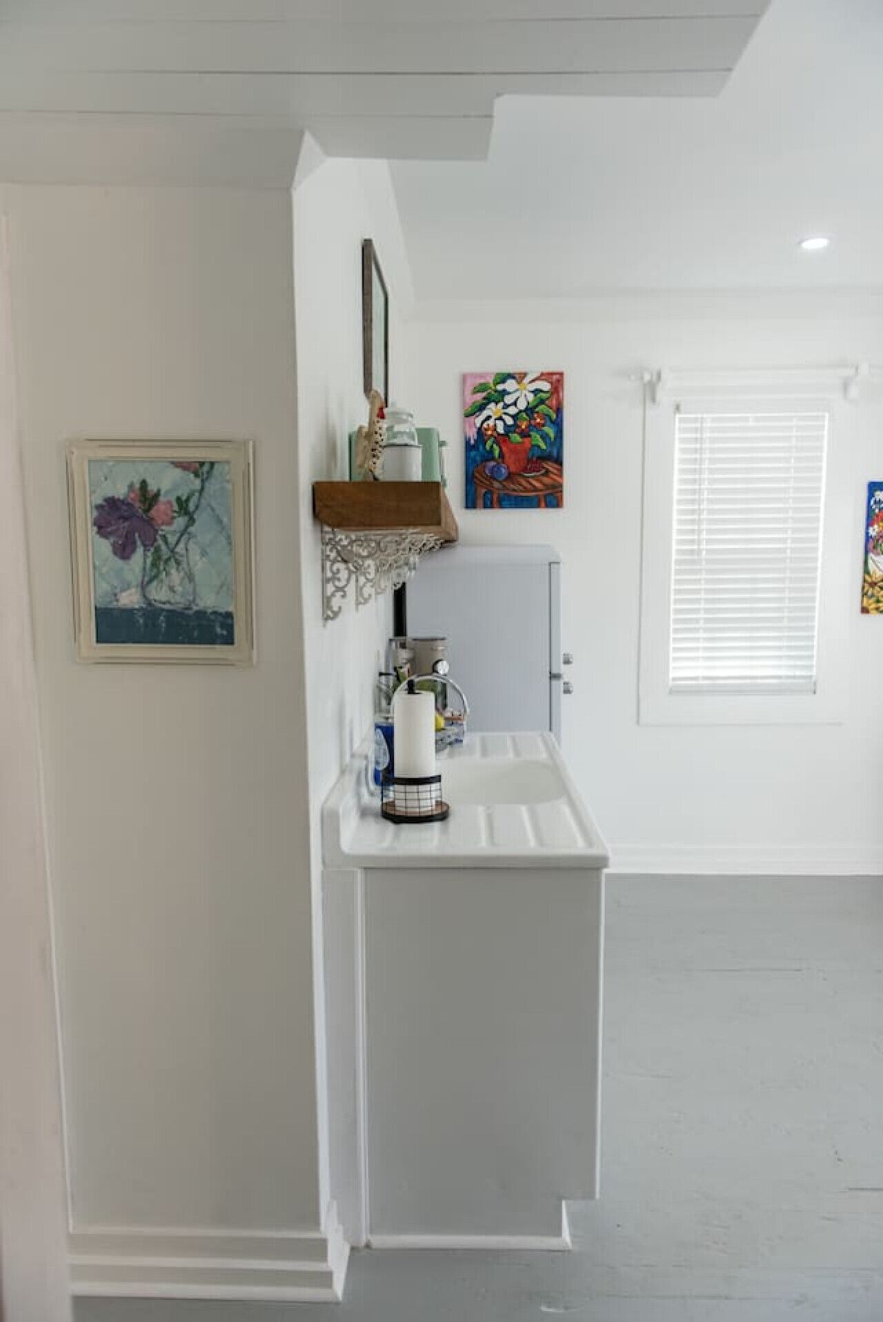 A white bathroom with a sink, a mirror, and two framed artworks on the wall.