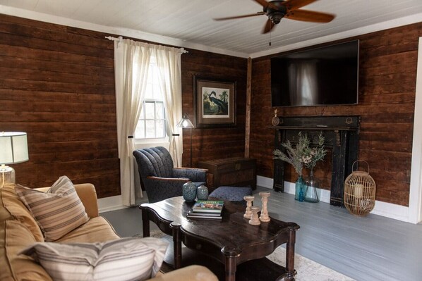 A cozy living room with a sofa, armchair, and coffee table. A fireplace with decorative items and a television mounted on the wall are also visible.