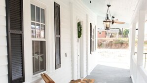 A covered porch with white wooden walls, black shutters, and a ceiling fan. - Little Noone by Raven’s Keep (Jackson)