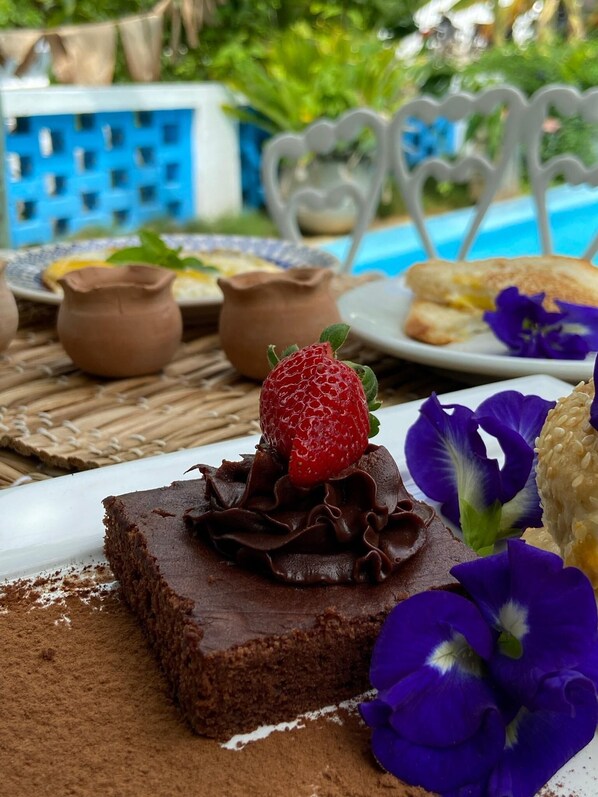 A dessert plate with chocolate cake, a strawberry, and purple flowers.