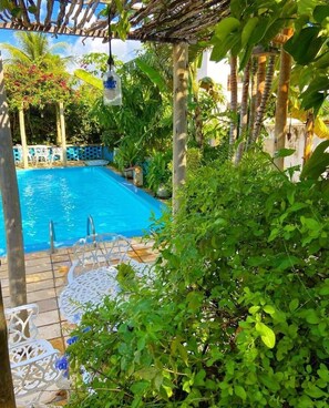 A pool area with a clear blue pool, surrounded by lush greenery and a pergola structure. - Pousada Vila Anauá (Japaratinga)