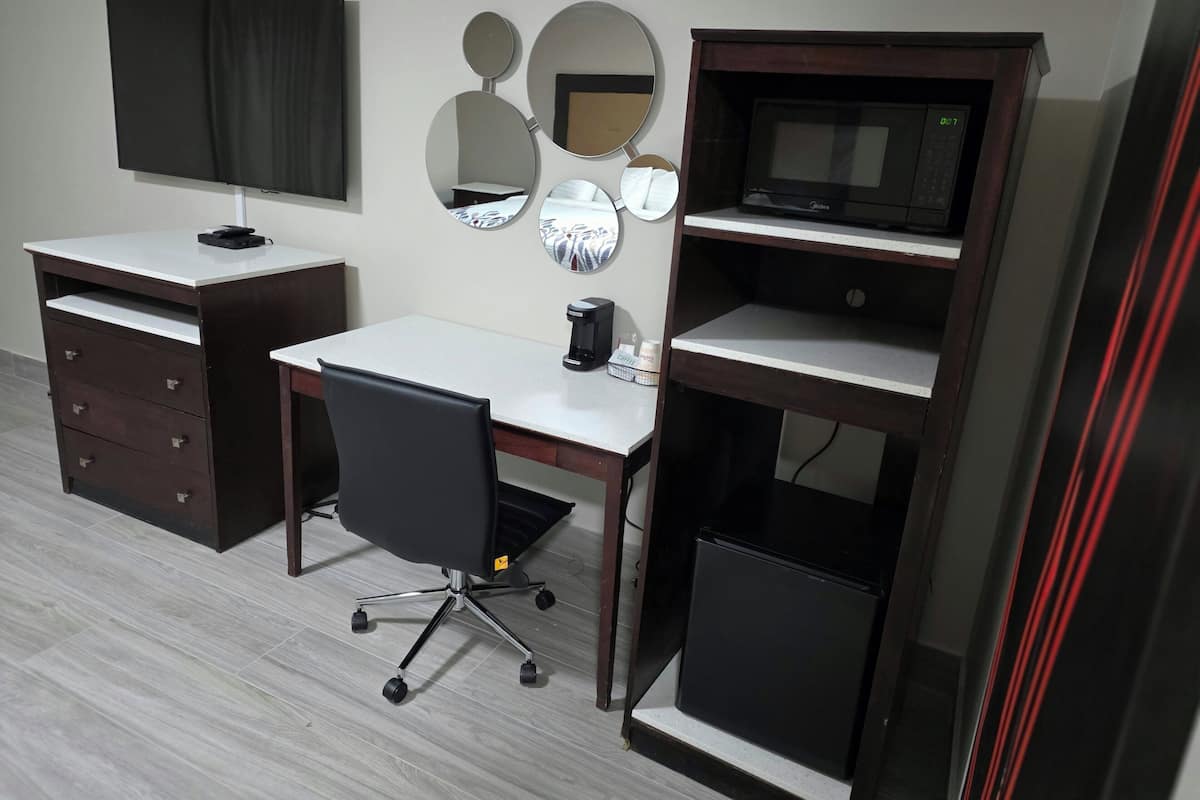 A room with a desk, chair, TV, and a coffee machine.