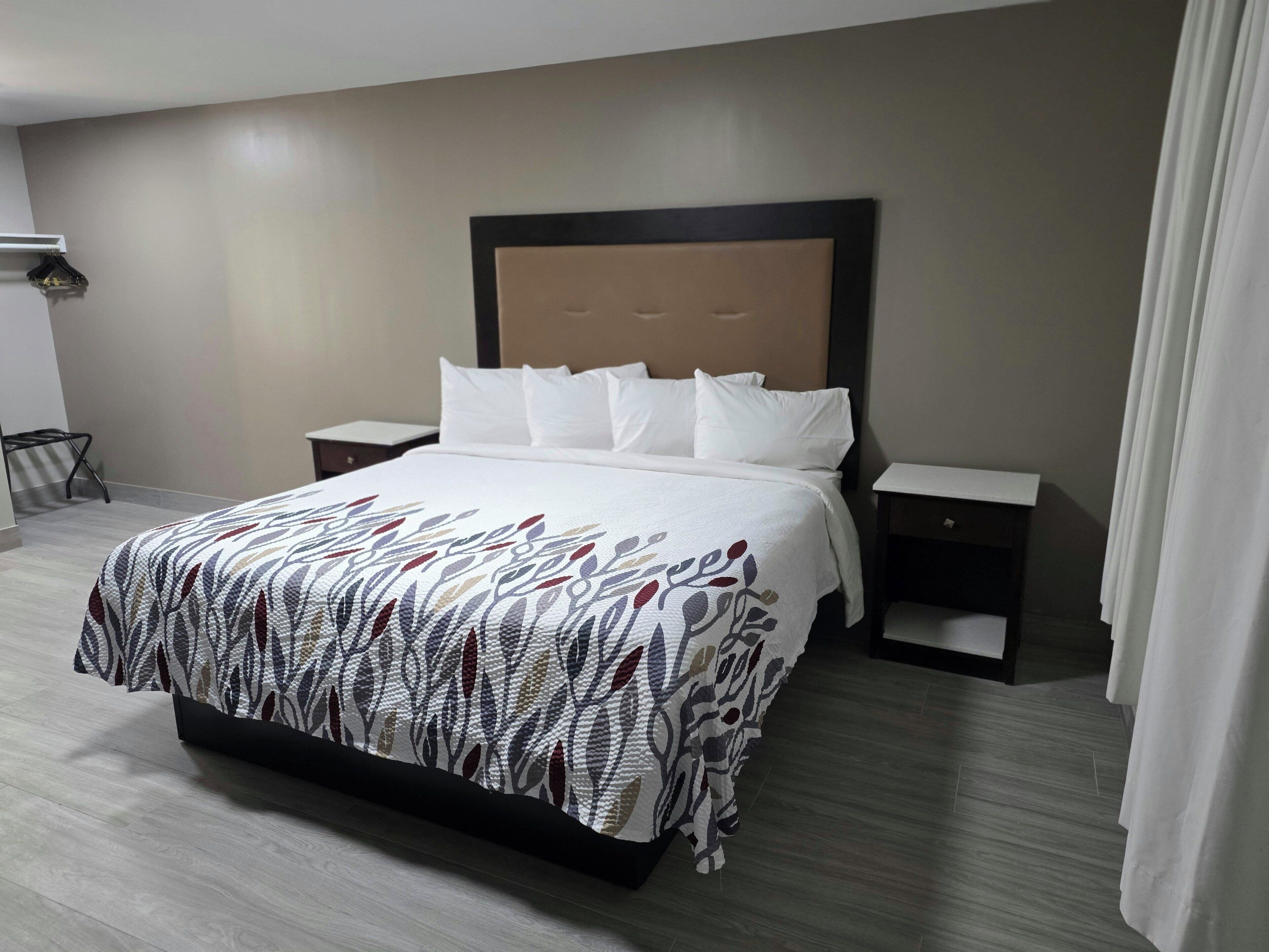 A hotel room with a bed, two bedside tables, a nightstand, and a wall-mounted lamp.