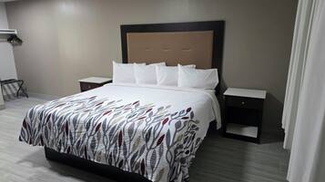 A hotel room with a bed, two bedside tables, a nightstand, and a wall-mounted lamp.