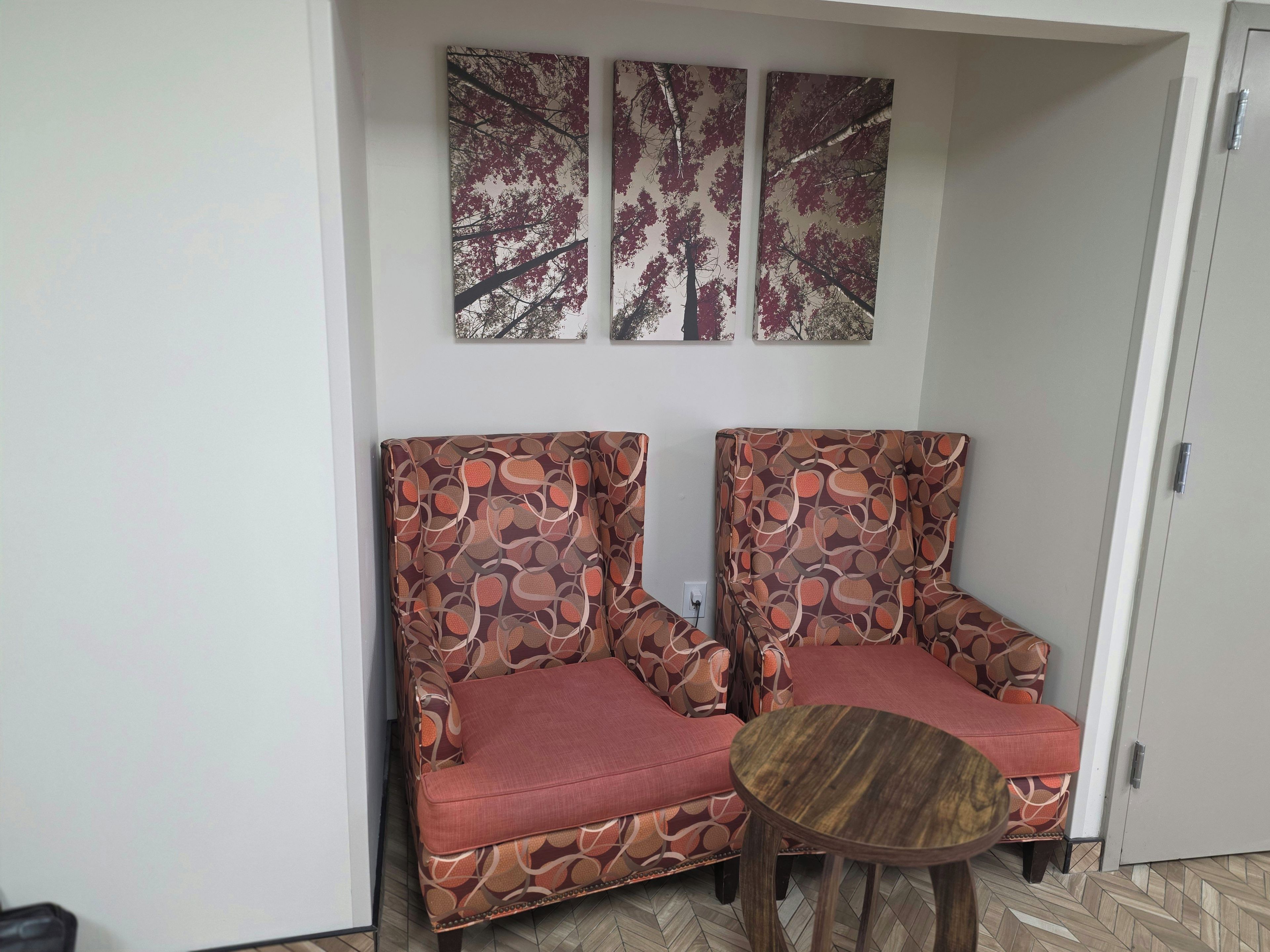 Ein Zimmer mit zwei gemusterten Sesseln, einem kleinen Holztisch und drei Wandbildern.