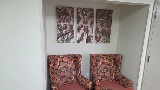 A room with two patterned armchairs, a small wooden table, and three wall-mounted artworks.