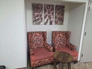 A room with two patterned armchairs, a small wooden table, and three wall-mounted artworks. - Red Roof Inn Green Brook - Somerset (Green Brook)
