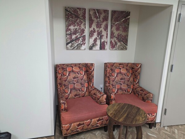 Una habitación con dos sillones estampados, una pequeña mesa de madera y tres obras de arte colgadas en la pared.
