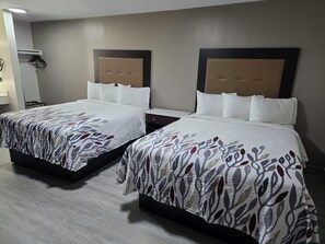 Two twin beds with patterned bedspreads, a wooden floor, and a wall-mounted light fixture. - Red Roof Inn Green Brook - Somerset (Green Brook)