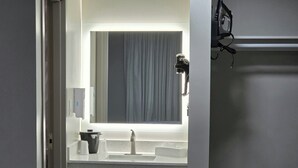 A bathroom with a mirror, sink, and a hairdryer on the counter.