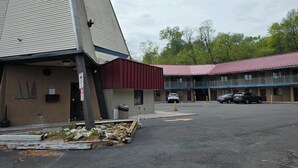 A motel with a red awning, a parking lot, and a building with a sloped roof. - Red Roof Inn Green Brook - Somerset (Green Brook)