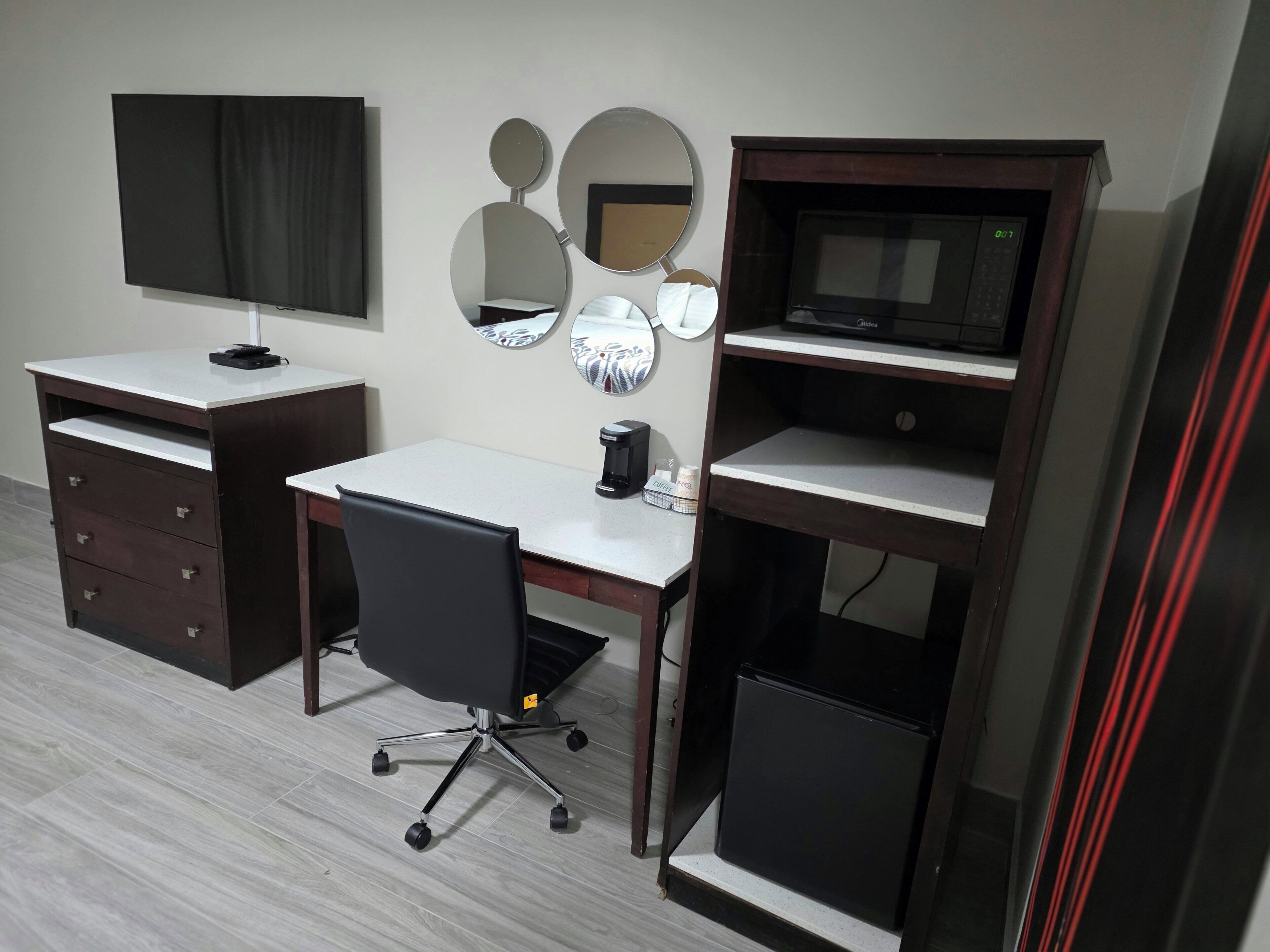Una habitación con escritorio, silla, televisión y cafetera.