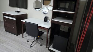 Una habitación con escritorio, silla, televisión y cafetera.