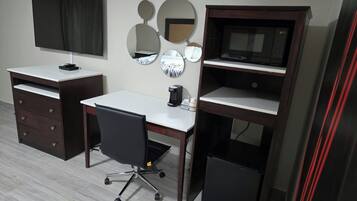 Una habitación con escritorio, silla, televisión y cafetera.