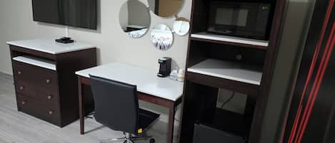 A room with a desk, chair, TV, and a coffee machine.