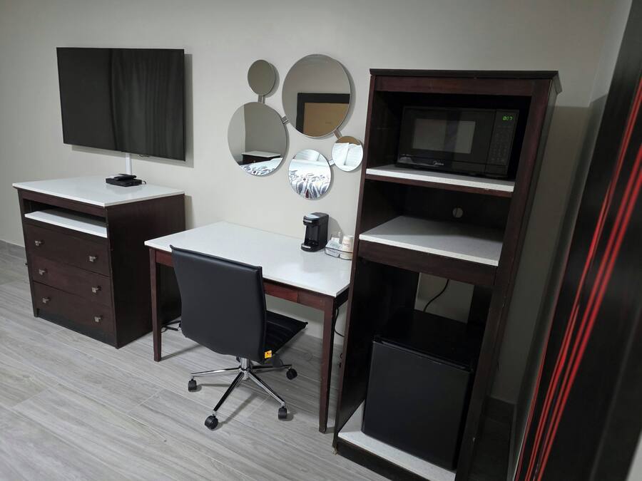 Quarto com escrivaninha, cadeira, televisão e máquina de café.