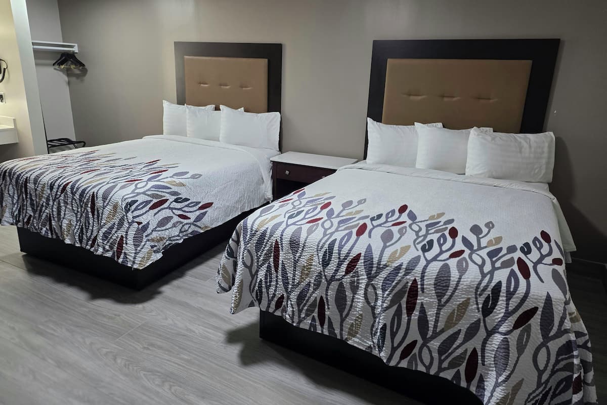 Two twin beds with patterned bedspreads, a wooden floor, and a wall-mounted light fixture.