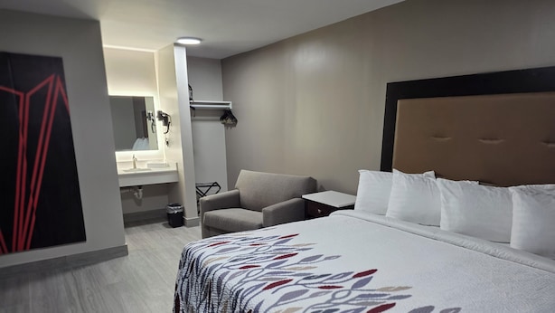 A hotel room with a large bed, a sofa, a small table, a mirror, and a bathroom. - Red Roof Inn Green Brook - Somerset (Green Brook)