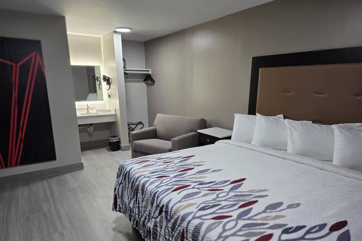 A hotel room with a large bed, a sofa, a small table, a mirror, and a bathroom.