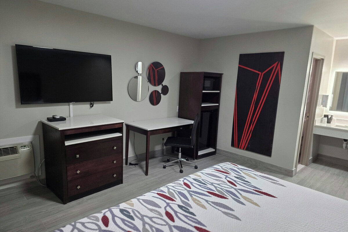 Una habitación de hotel con cama, escritorio, televisor, armario y baño.