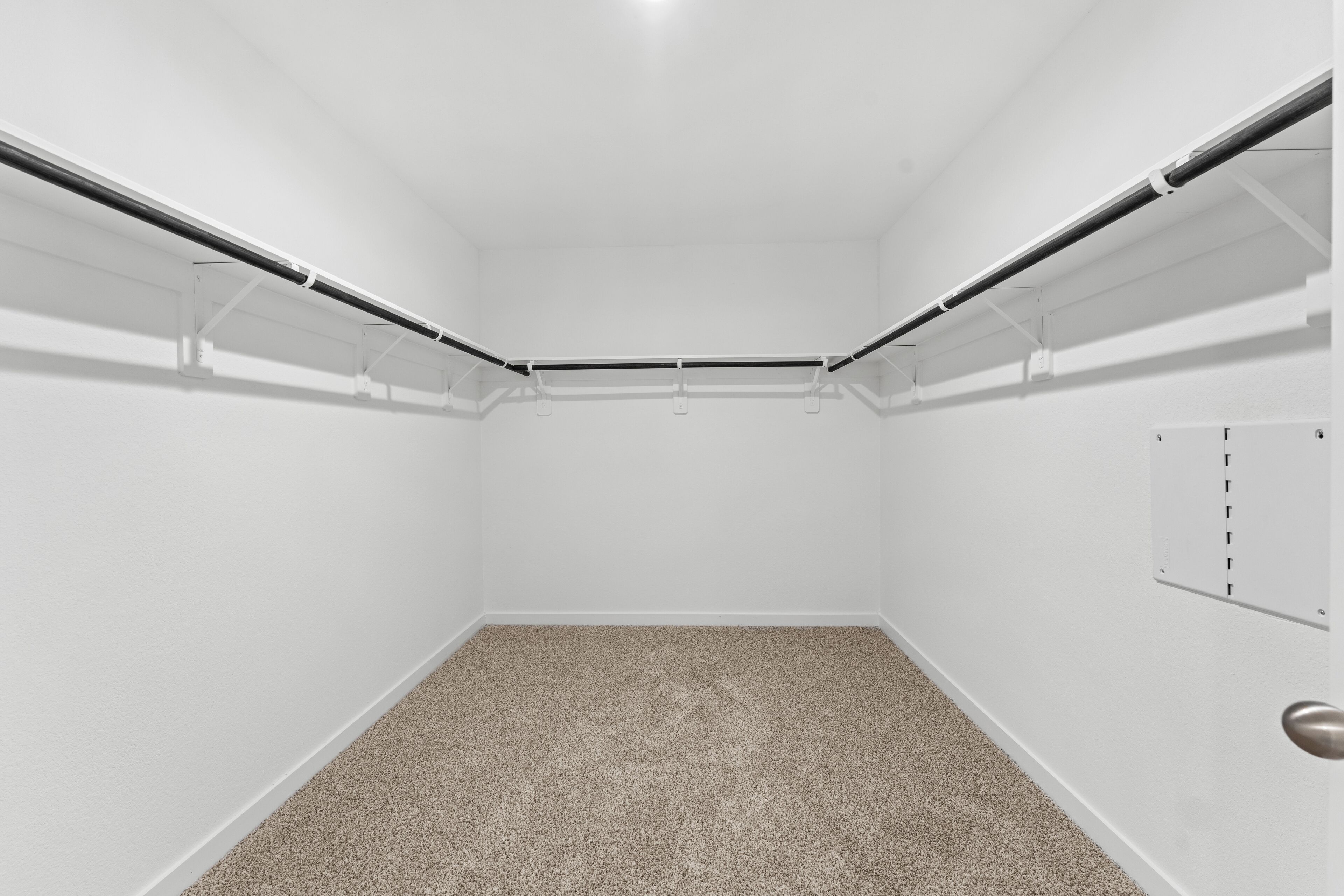 Un placard d’angle avec un tapis beige, des murs blancs et une porte en métal.