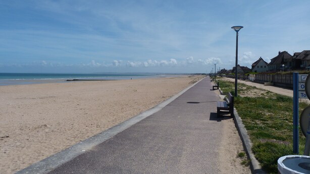 A paved walkway along a beach with benches and a lamppost.