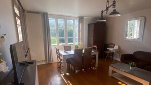 A spacious living room with a wooden floor, a dining area with a table and chairs, a sofa, and a television on a stand.