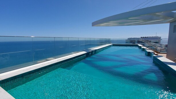 Una piscina infinita de color azul intenso con barandilla de cristal que ofrece vistas al mar.