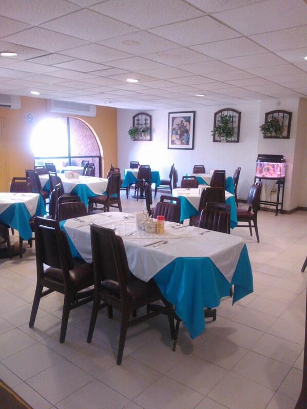 Un espace repas avec des tables recouvertes de nappes blanches et agrémentées de chemins de table bleus, disposées en rangées avec des chaises.